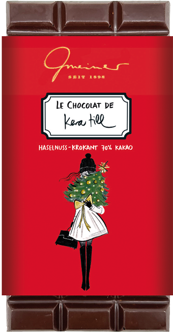 Gmeiner Schokolade Kera Till Schokoladentafel in roter Verpackung mit eleganter Frau, Weihnachtsbaum vor Gesicht, Mantel, Stiefeln und Handtasche.