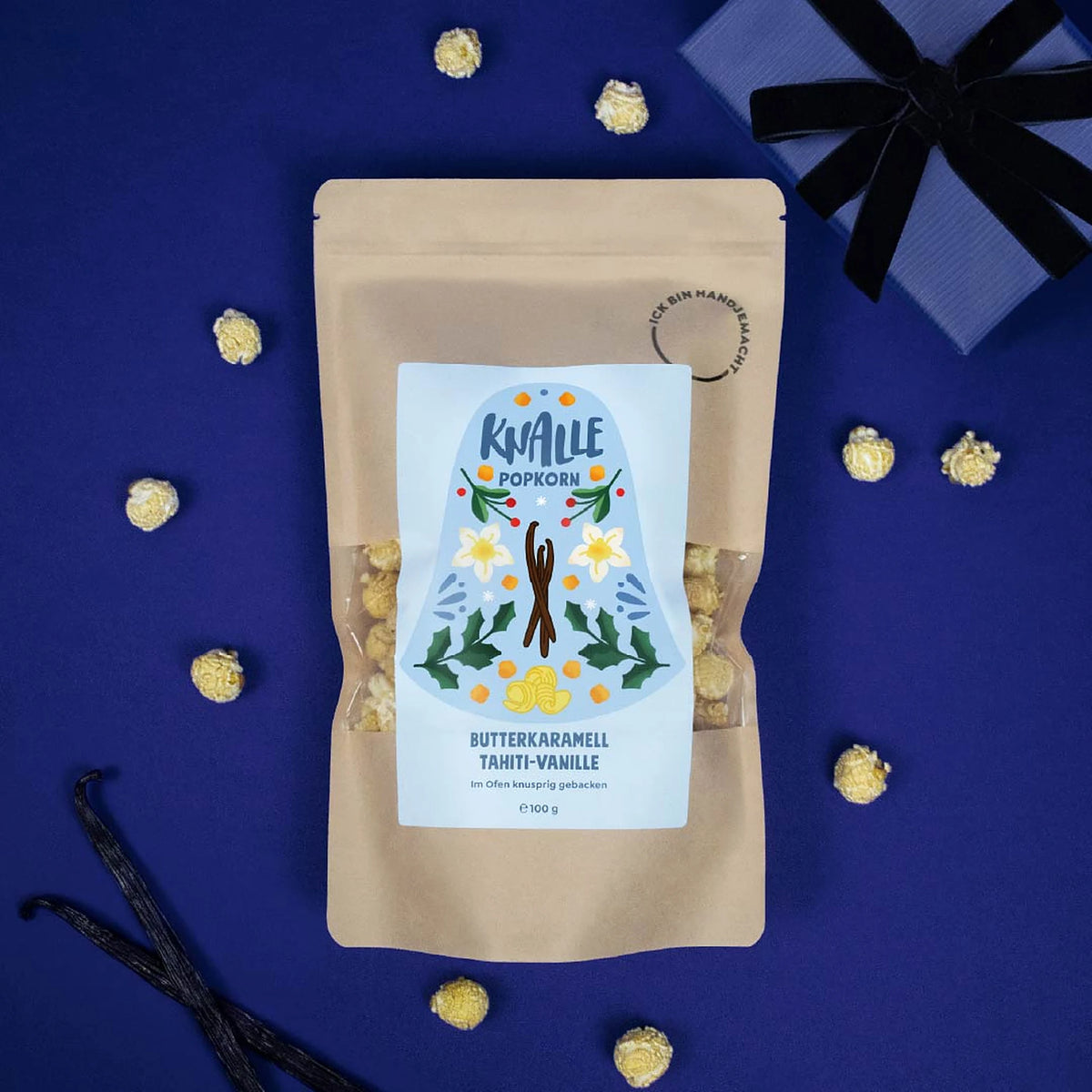 Knalle Popcorn Butterkaramell Tahiti-Vanille Winteredition mit Vanilleschoten und Geschenk auf blauem Hintergrund