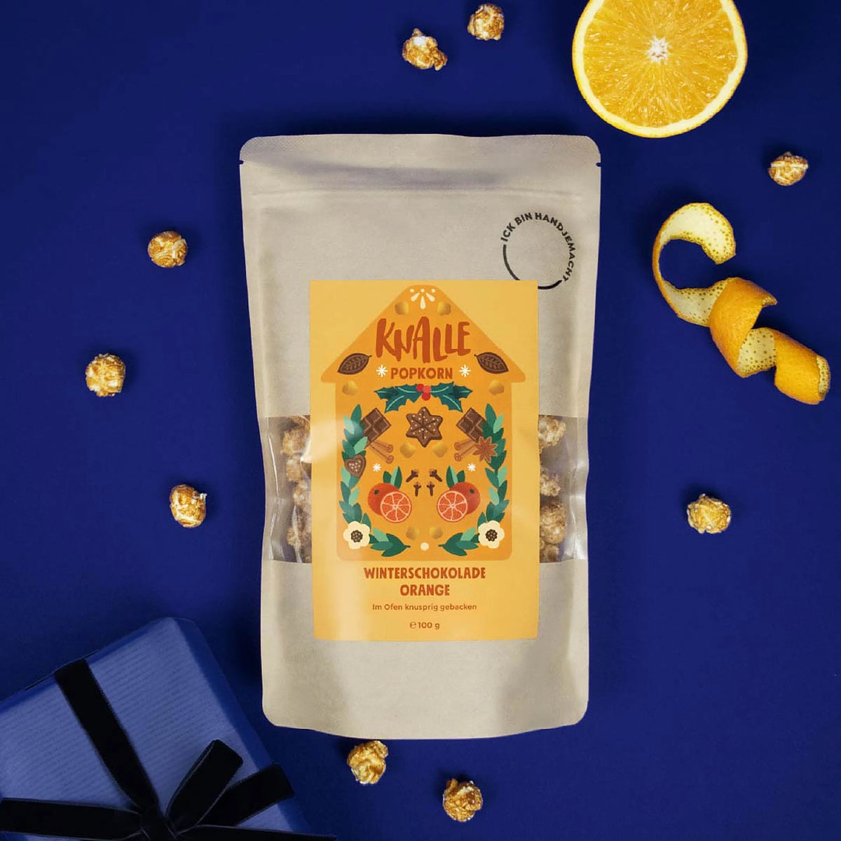 Knalle Popcorn Winterschokolade Orange mit Orangenhälfte und Orangenschale auf blauem Hintergrund
